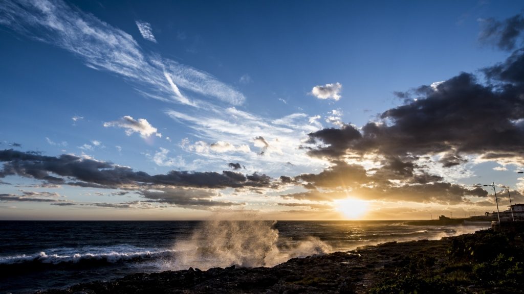  sun rising out of the sky through the clouds under a blue sky over a dimly lit beach