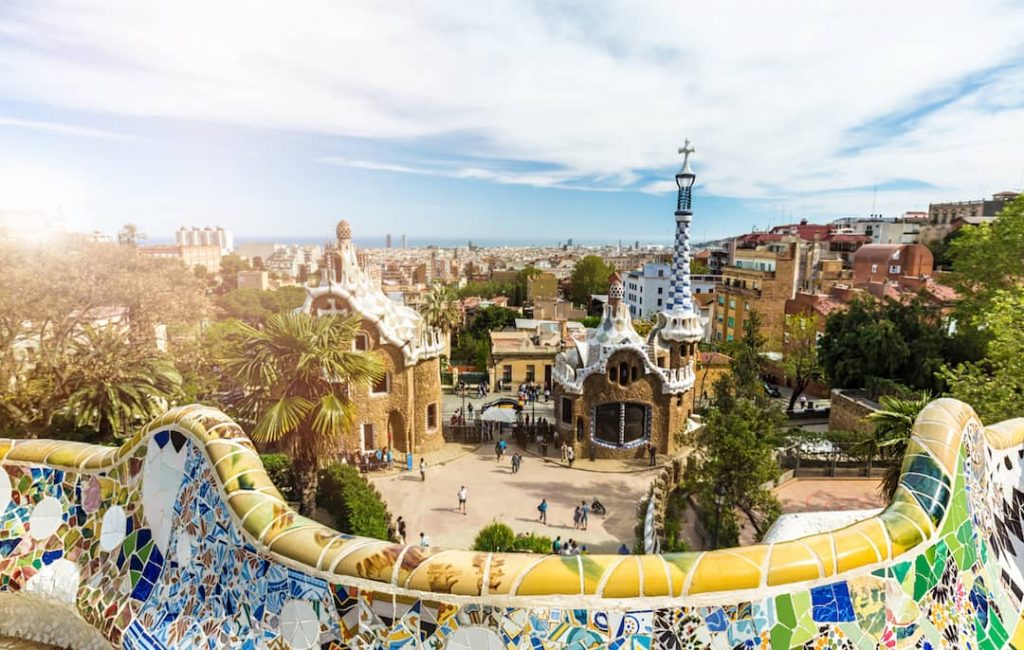 Shot of Barcelona showcasing some of it's unique architecture: a colourful mosaic wall, green trees and eclectic looking buildings