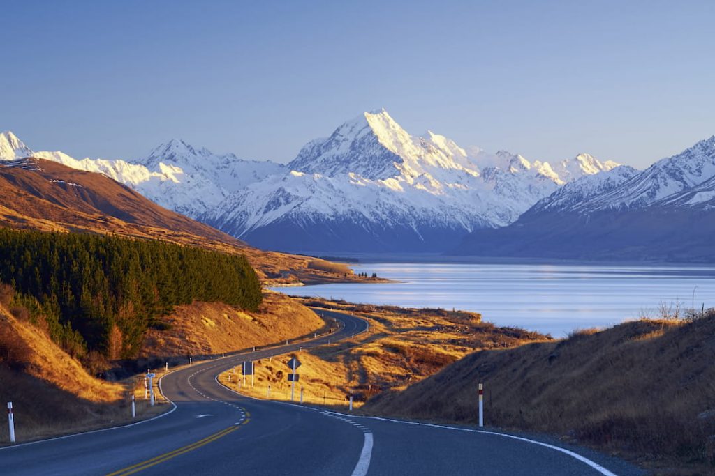 a highway snakes through new zealand's country side alongside a valley with a lake and mountains 