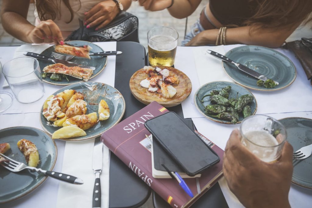 small plates of food sit on a table as a group pf people's hands are seen munching on food