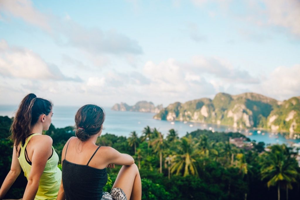 Two women sitting on a cliff, looking down at the Phi Phi Islands, Thailand