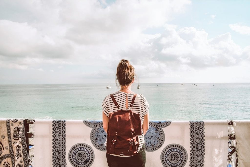 A girl in a black and white striped shirt stands with her back to the camera, looking out at the ocean in Monterosso al Mare, Italy