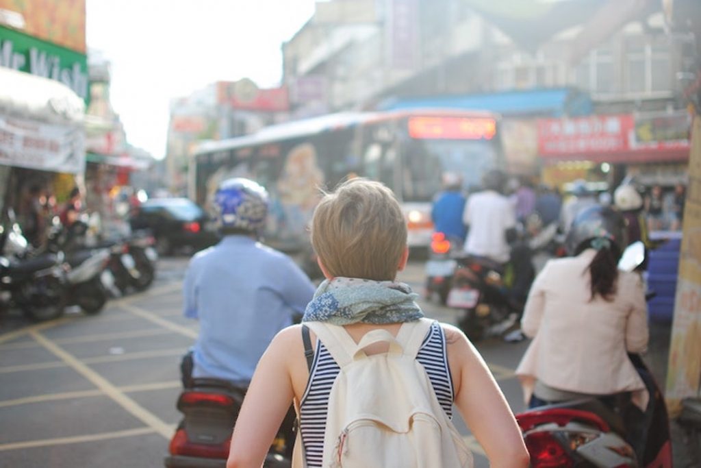 Solo traveller with a backpack stands in the middle of a crowded street