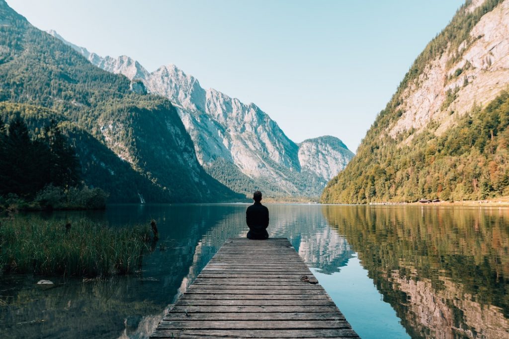 Man sits in a valley looking out at a water body