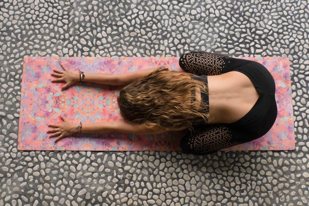 a woman in child's pose on a pink yoga mat on top of cobblestones