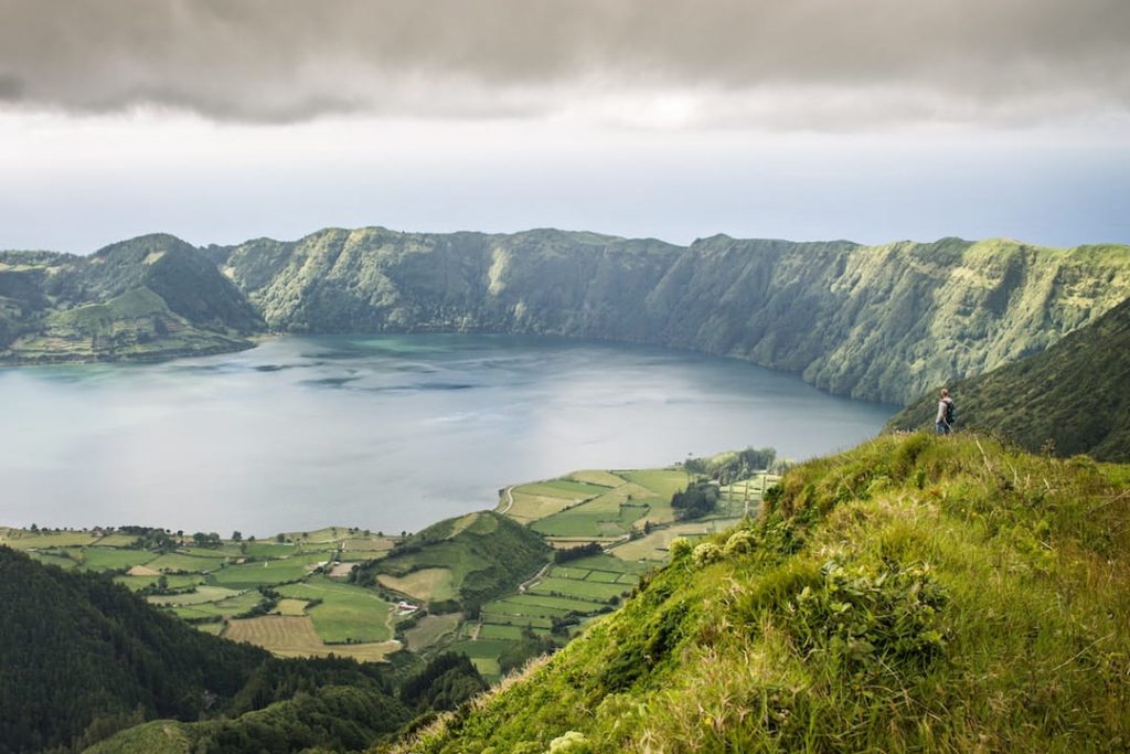 A man standing alone in a field overlooking a lake in Sao Miguel, Portugal