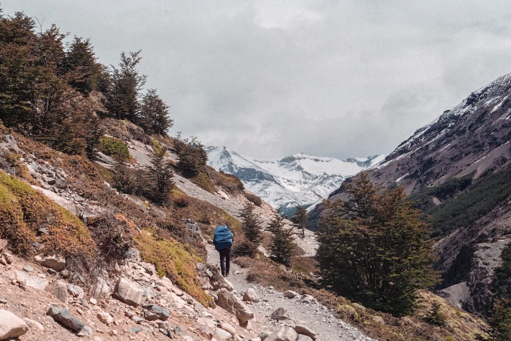 homme en veste bleue en randonnée sur un sentier avec des montagnes enneigées en arrière-plan