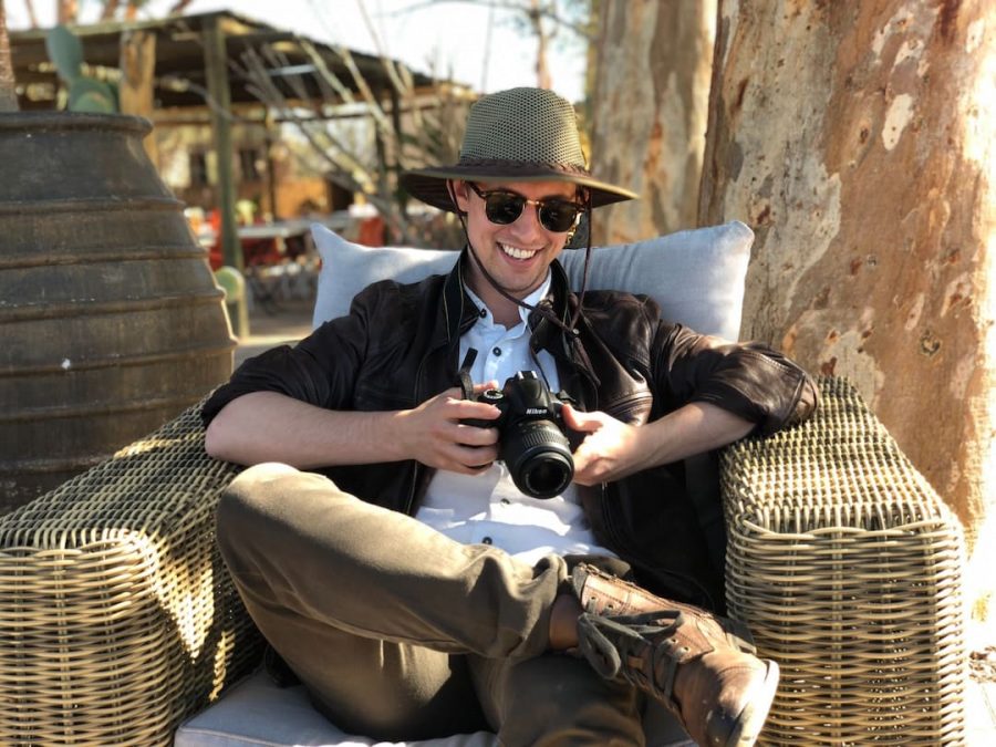 A person sitting in a chair crossed legged smiling looking at his camera 