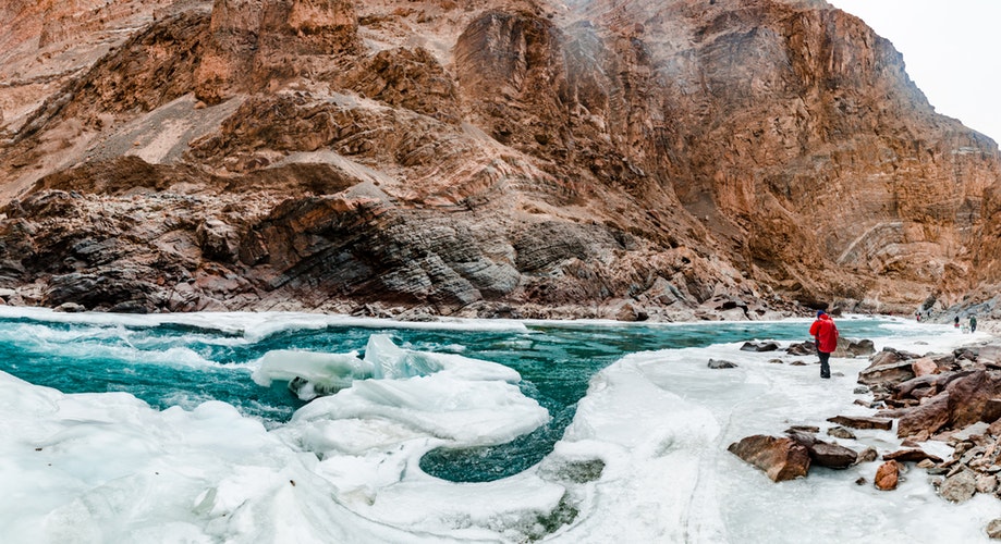 hiker traversing a sheet of ice beside the water