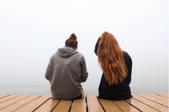 Two women sitting on a dock on a foggy day