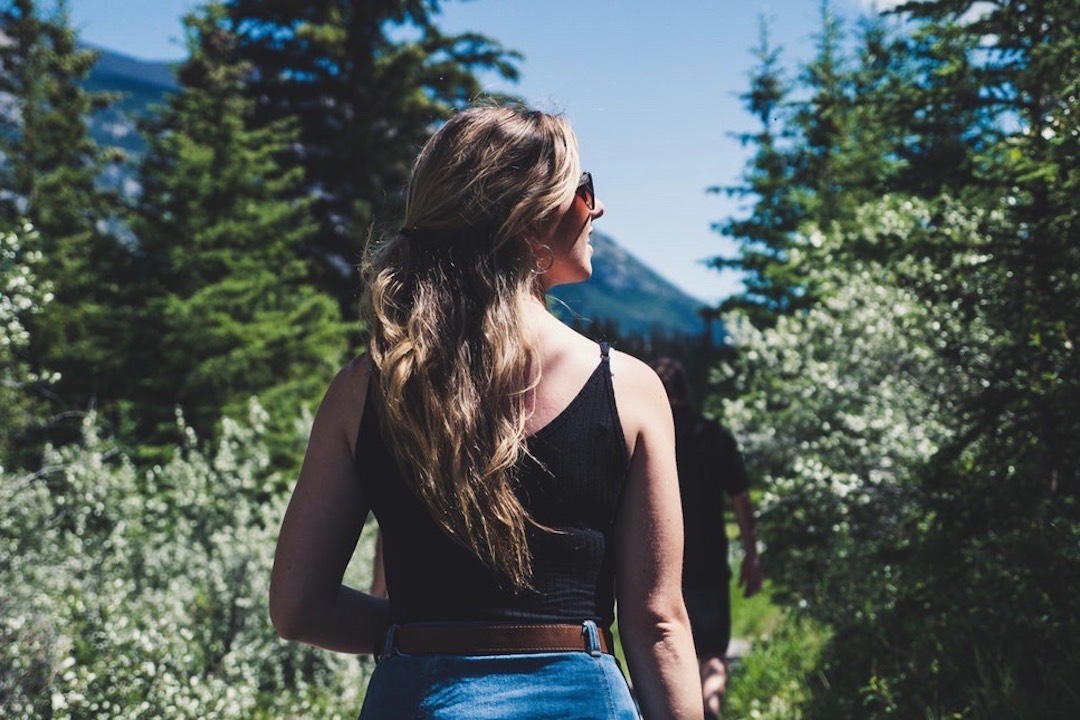 woman wearing black spaghetti strap crop top standing in front of trees while looking left side during daytime