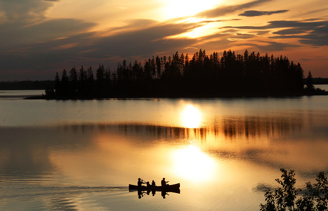 a group of people sail along a lake during sunset in sepia tones of yellow and orange