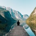 A man sitting on the edge of a dock facing a mountain in Germany