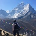 climber with a backpack stands in front of mountain peaks with colourful flags