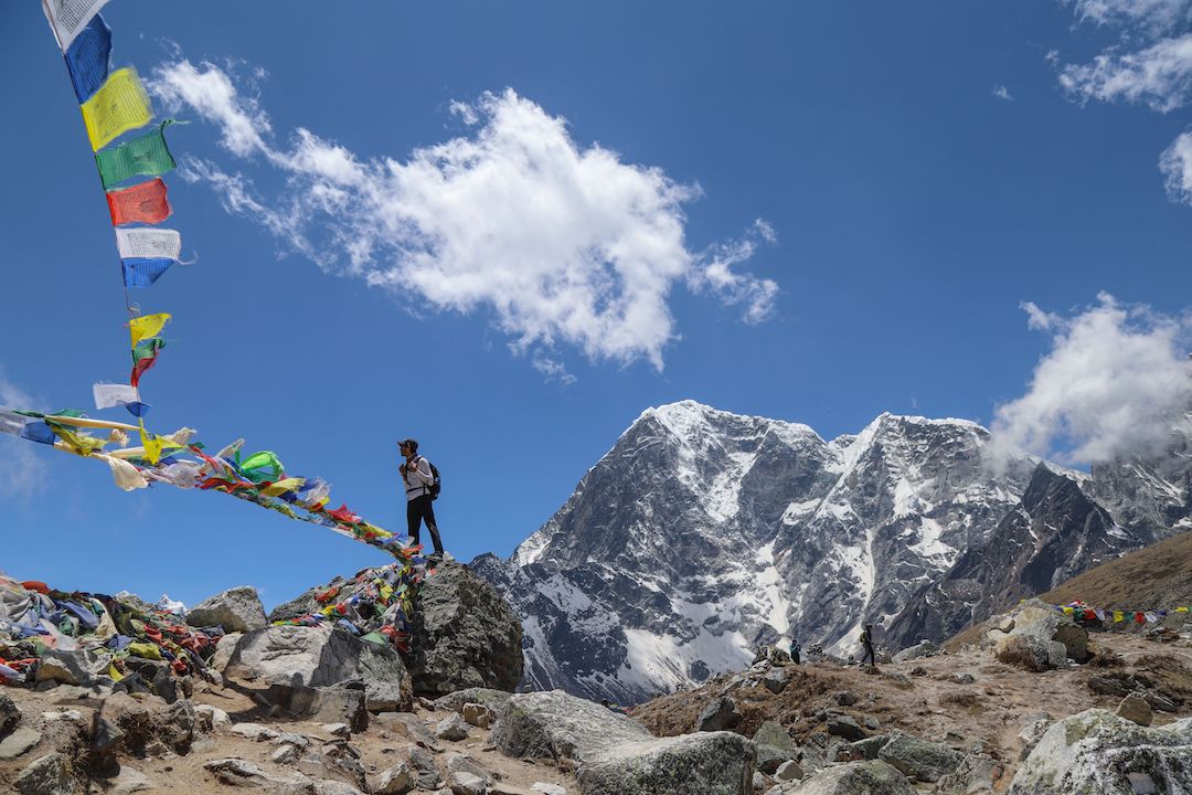 a man standing in a mountain range with colourful flags fluttering in the air