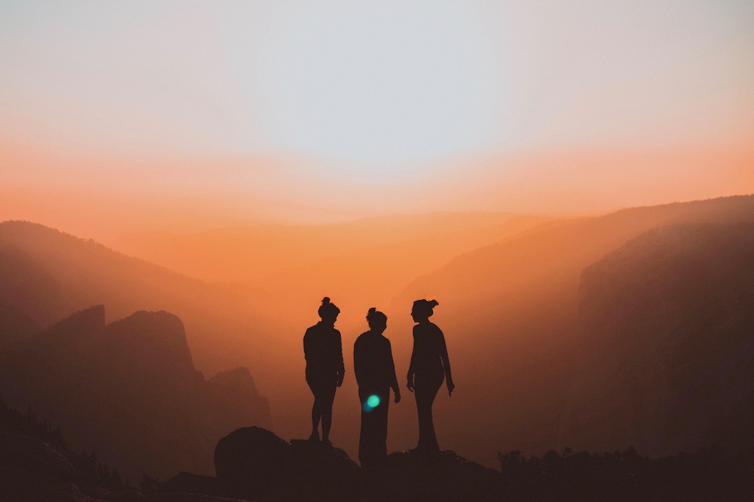 silhouette of three women standing in an orange sunset