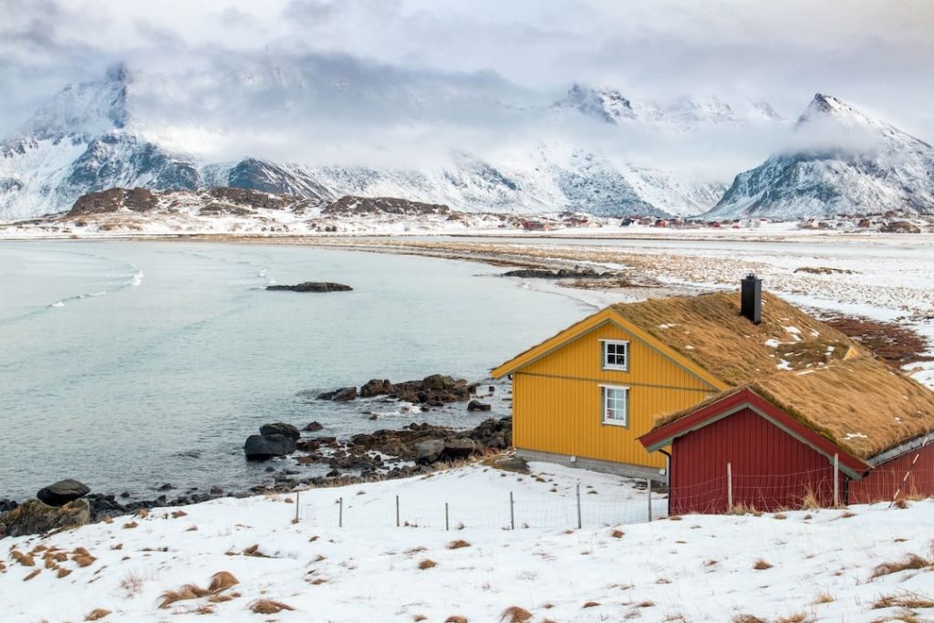 A traditional red and yellow house on the water with mountains in the background in the Lofoten Islands, Norway