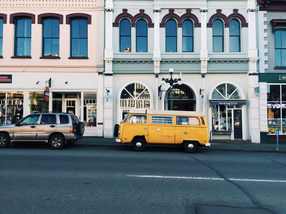 yellow van behind silver SUV in front of boutiques