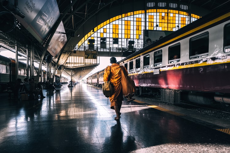 monk in traditional robes walking on railway station platform near trai