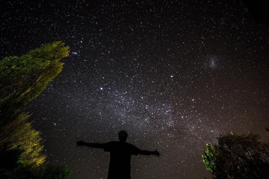 Person standing with their arms spread staring at the starry night sky