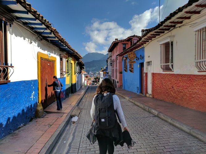 person in gray shirt with backpack walking on street between houses