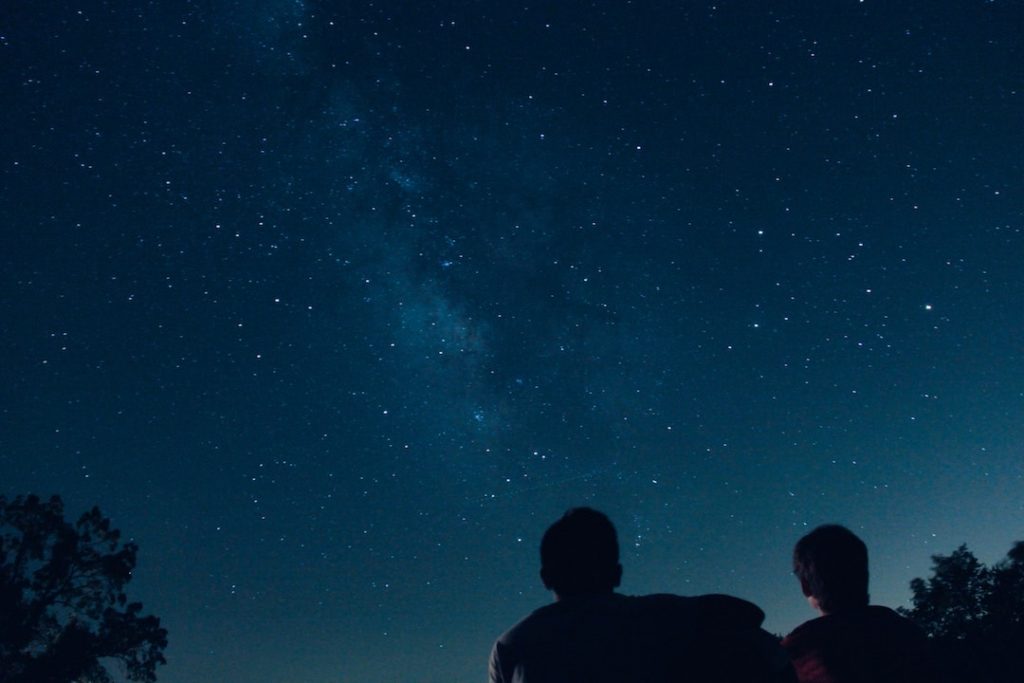 Two people sitting on the ground gazing up at the starry night sky