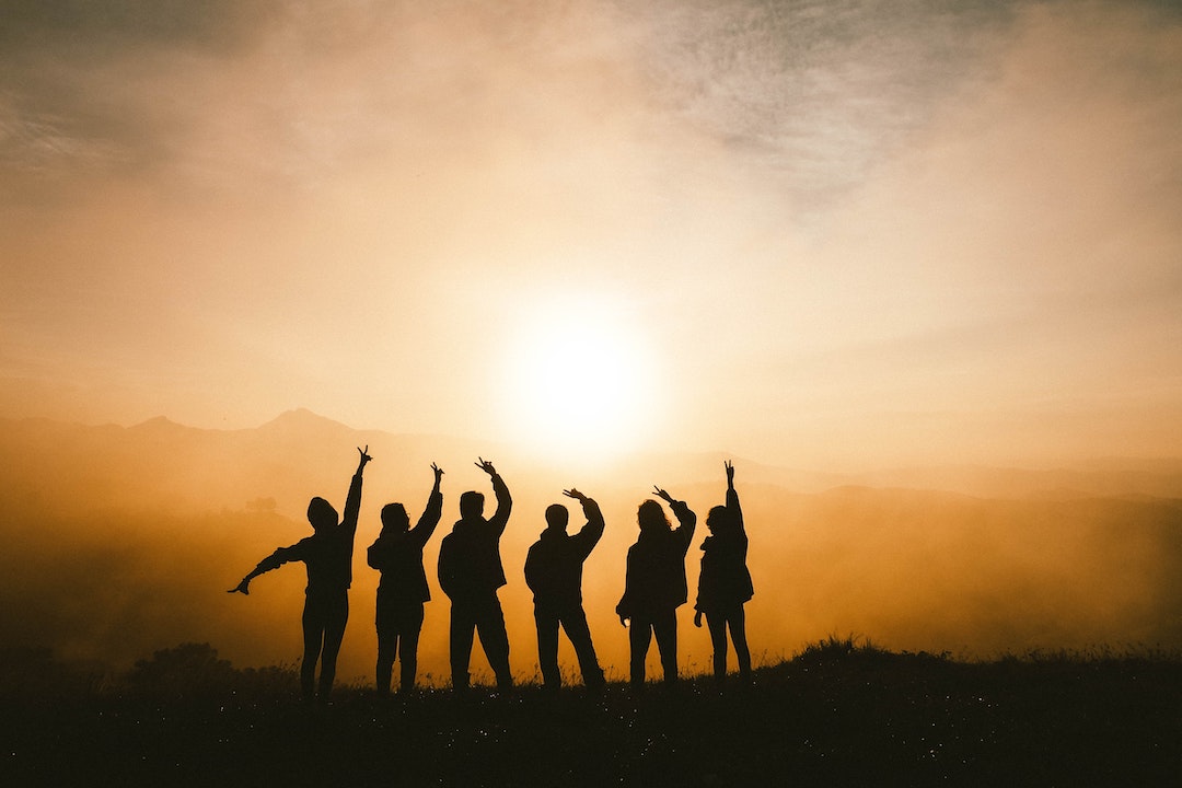 Silhouette of a group of people giving the peace sign in front of a sunset