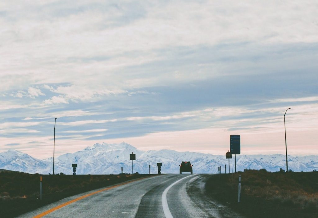 Single car on a road with snow capped peaks in the distance