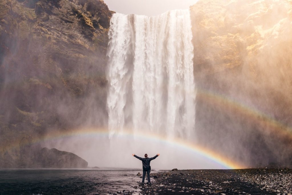 Person standing in front of waterfall and rainbow in Iceland