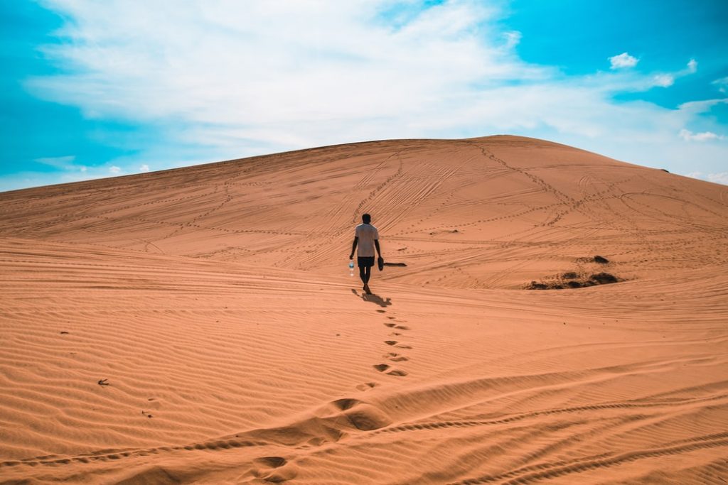 man walking across a sand dune barefoot