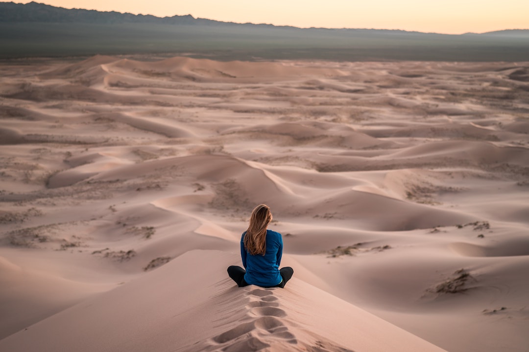 Woman sitting with her back facing camera on a sand dune