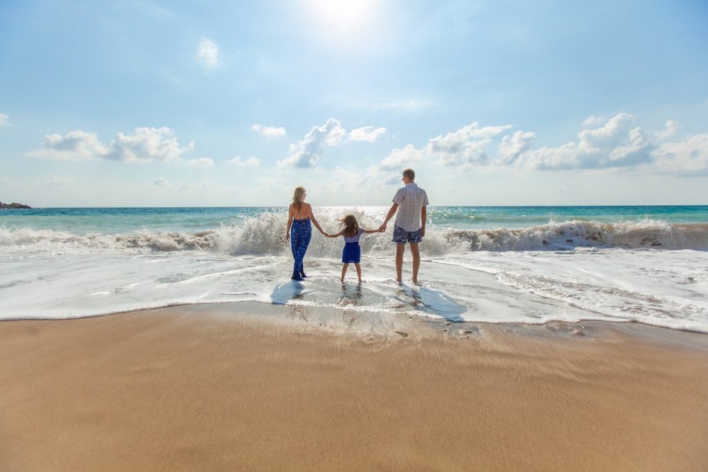 Family of three holding hands walking into the ocean on a beach