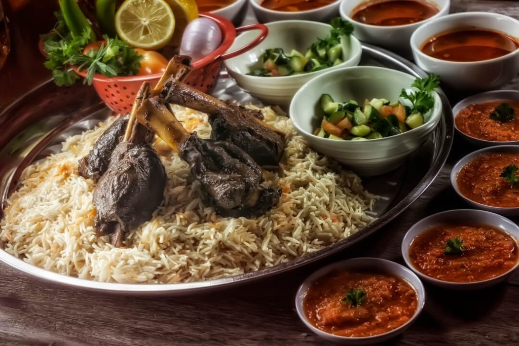 A food image showing a traditional Saudi Arabian meal with lamb and side dishes