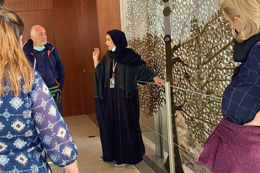 Female Saudi tour guide dressed in an abaya talks to her tour group.