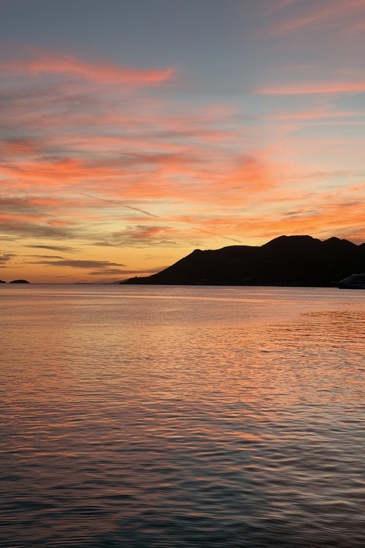 Orange and pink sunset over calm sea and a dark island silhouette near Korcula, Croatia