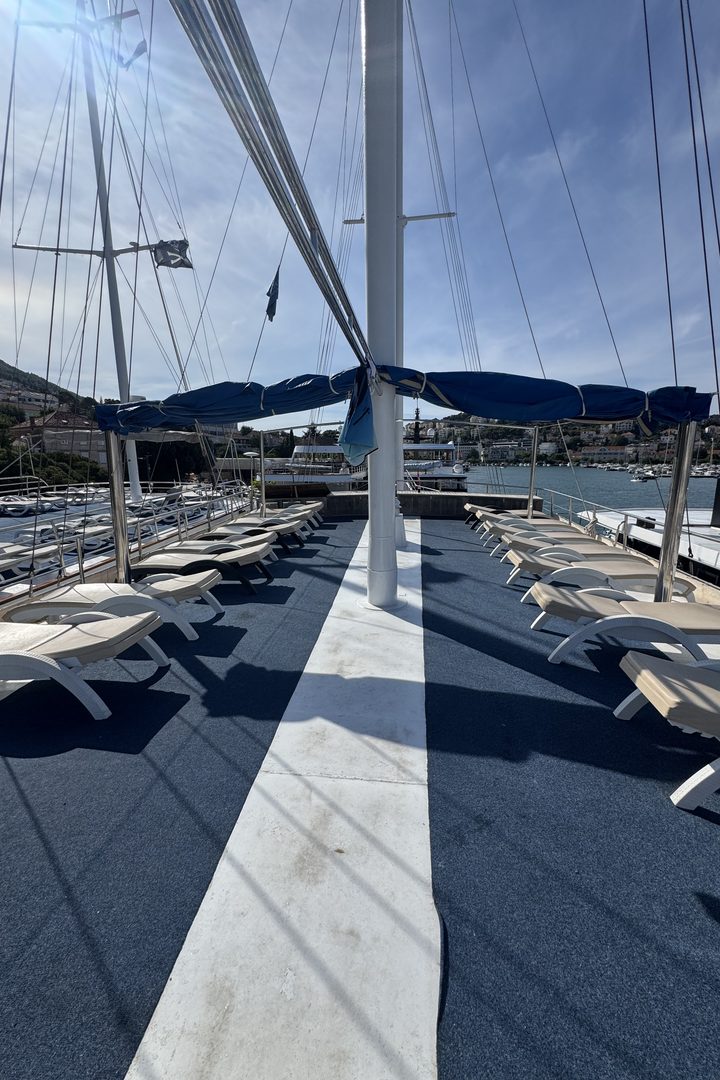 Rows of white sunbeds under a blue awning on the deck of a sailing boat in Croatia, with masts and rigging overhead