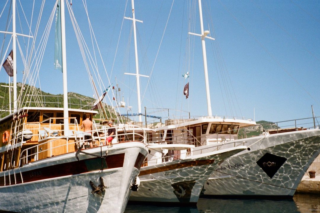 Traditional wooden sailing boats moored side by side in a Croatian harbor under a clear blue sky