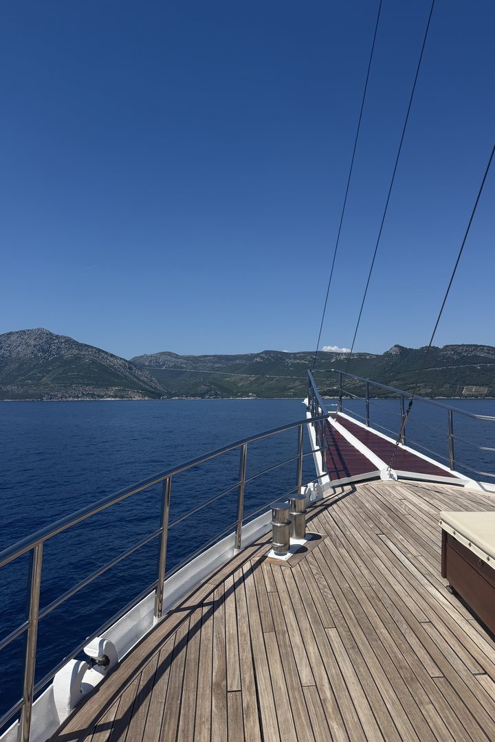 View along the wooden bow of a sailing boat toward green islands across deep blue Adriatic water in Croatia