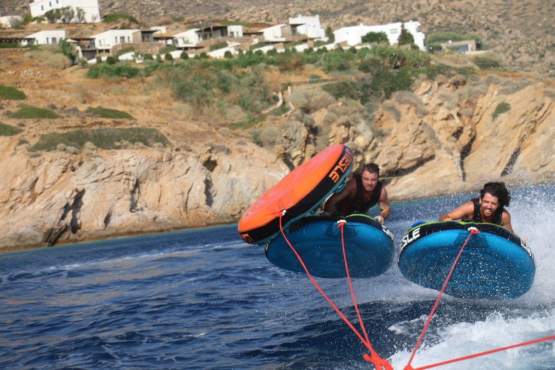 Two travelers on inflatable tubes being pulled across the water off the rocky coast of Ios, Greece