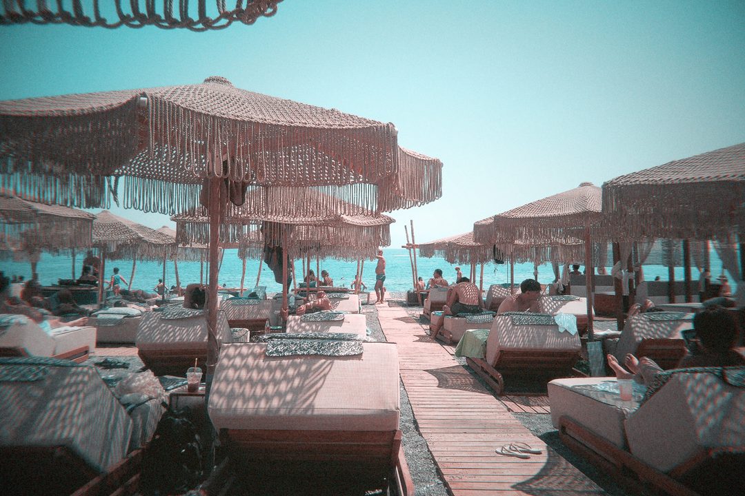 Rows of cushioned sunbeds under fringed straw umbrellas at a beach club in Santorini, Greece